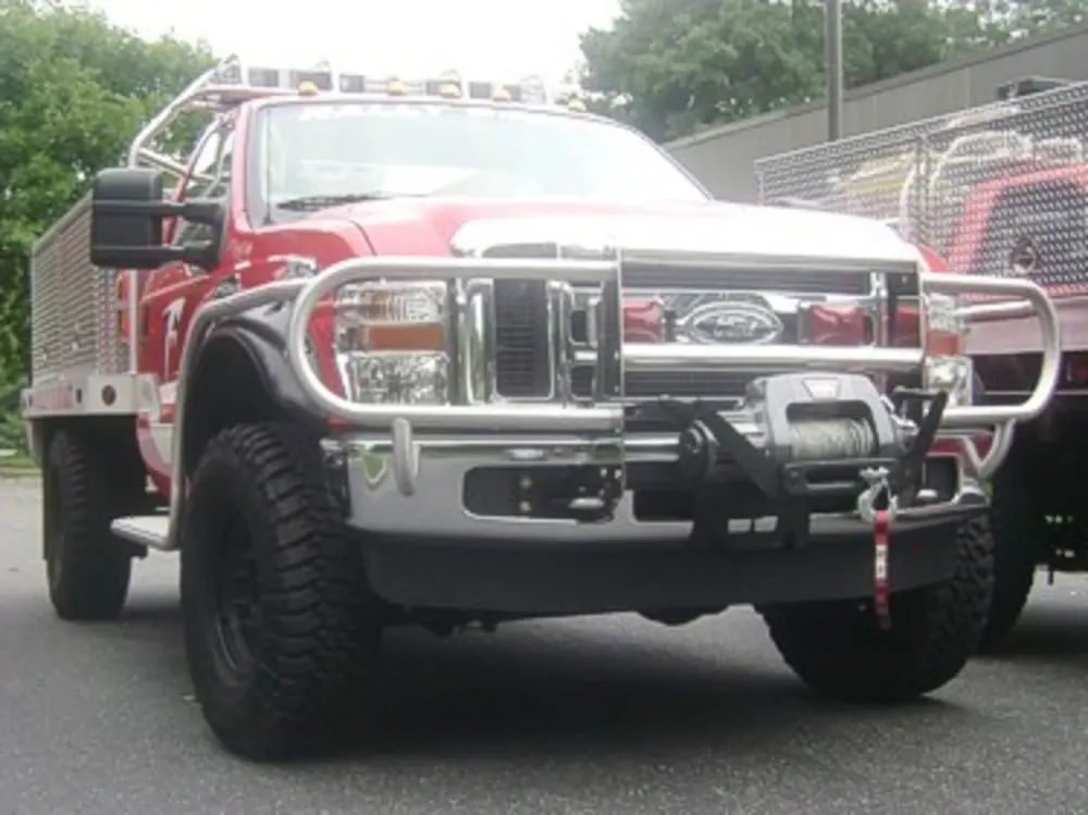 Exterior view of small fire truck showing cab, body compartments, and wheel/tire area.