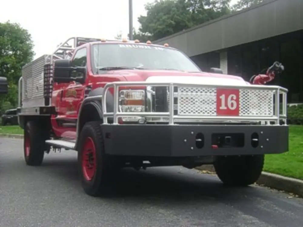 Exterior view of small fire truck showing cab, body compartments, and wheel/tire area.