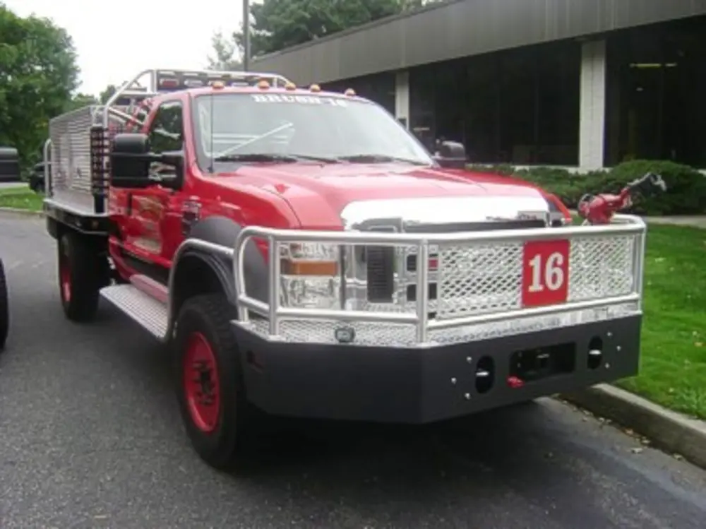 Exterior view of small fire truck showing cab, body compartments, and wheel/tire area.