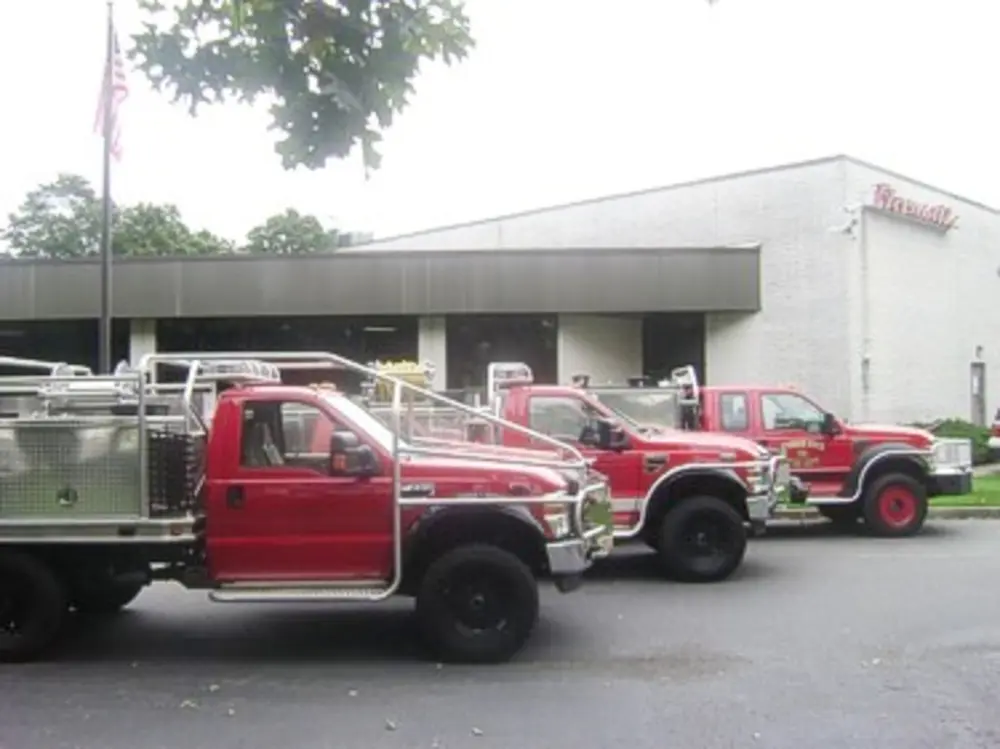 Exterior view of small fire truck showing cab, body compartments, and wheel/tire area.