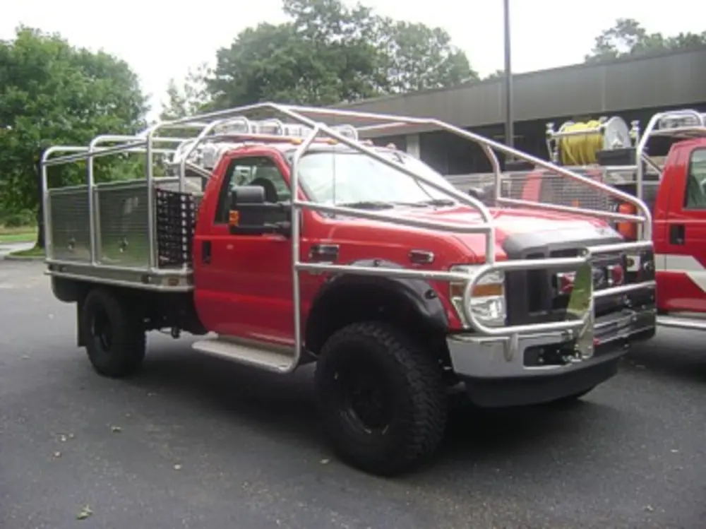 Exterior view of small fire truck showing cab, body compartments, and wheel/tire area.