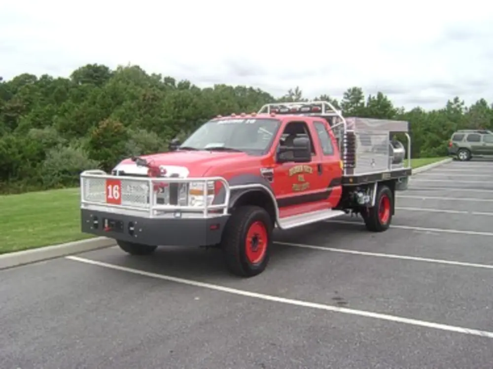 Exterior view of small fire truck showing cab, body compartments, and wheel/tire area.