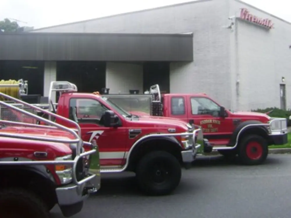 Exterior view of small fire truck showing cab, body compartments, and wheel/tire area.