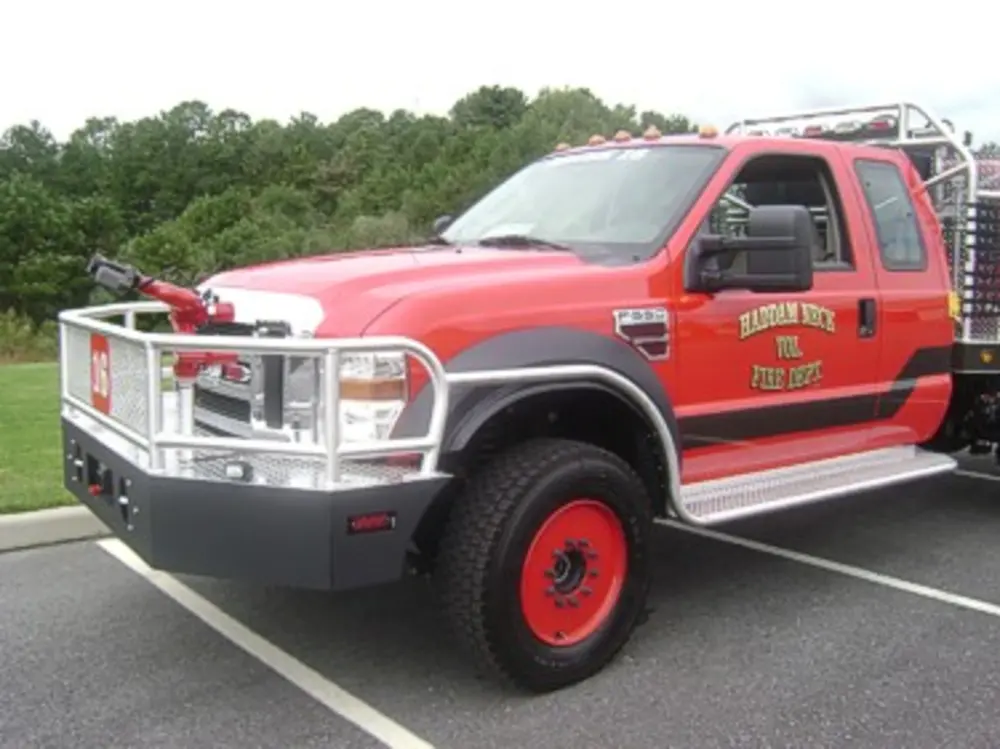 Exterior view of small fire truck showing cab, body compartments, and wheel/tire area.