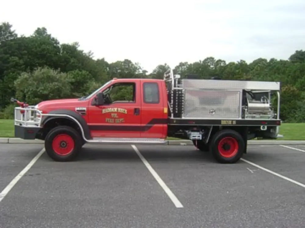 Exterior view of small fire truck showing cab, body compartments, and wheel/tire area.