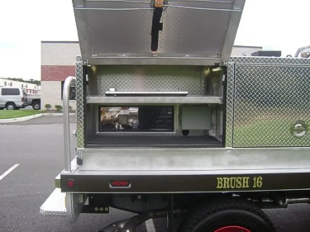 Exterior view of small fire truck showing cab, body compartments, and wheel/tire area.