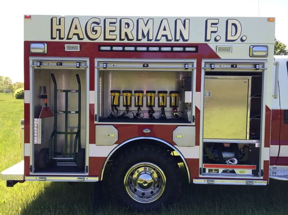 Exterior view of small fire truck showing cab, body compartments, and wheel/tire area.
