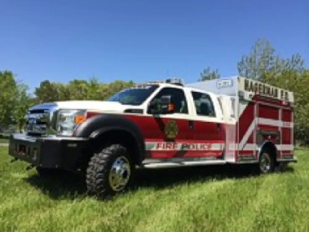 Exterior view of small fire truck showing cab, body compartments, and wheel/tire area.