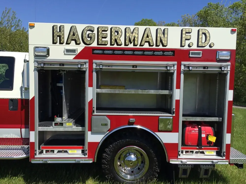 Exterior view of small fire truck showing cab, body compartments, and wheel/tire area.