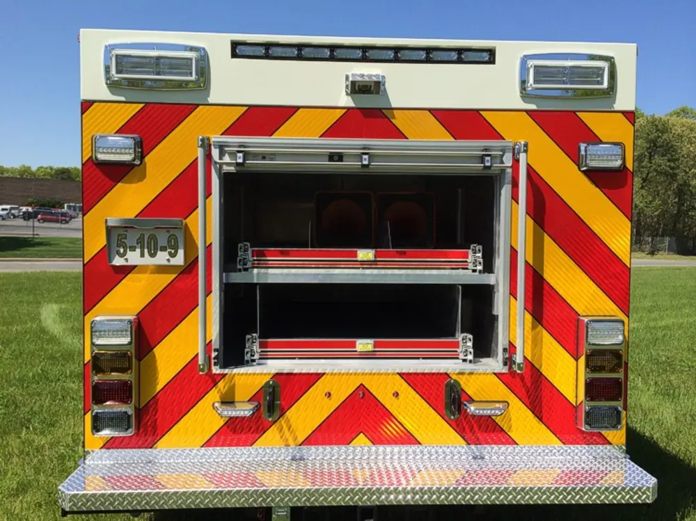 Exterior view of small fire truck showing cab, body compartments, and wheel/tire area.