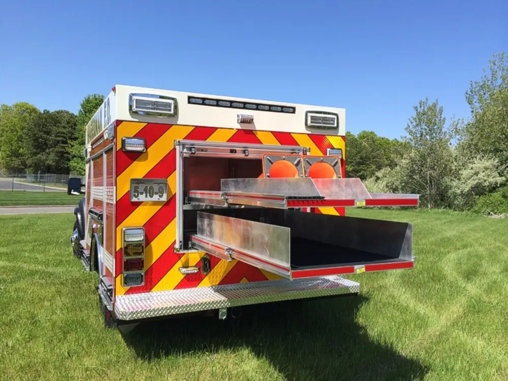 Exterior view of small fire truck showing cab, body compartments, and wheel/tire area.