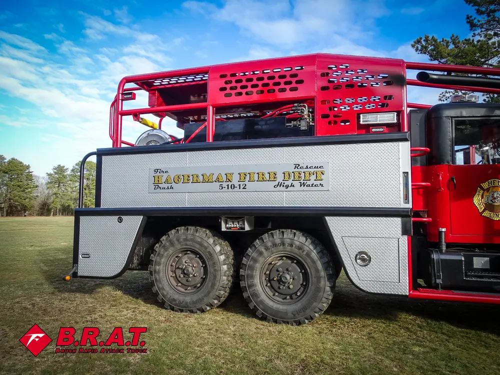 Exterior view of small fire truck showing cab, body compartments, and wheel/tire area.