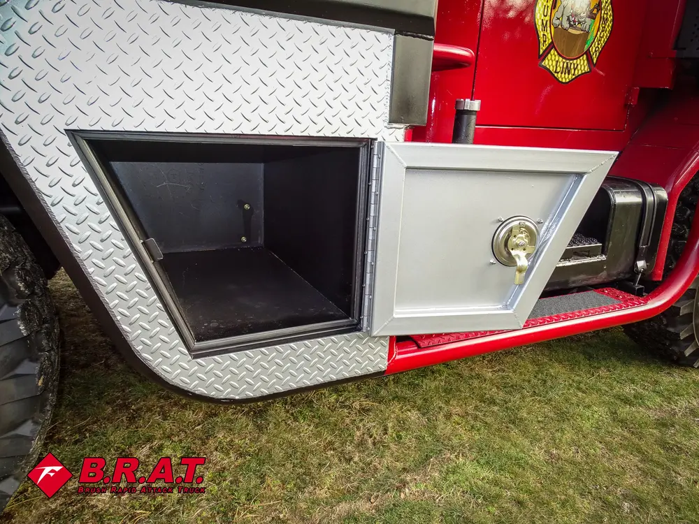 Exterior view of small fire truck showing cab, body compartments, and wheel/tire area.