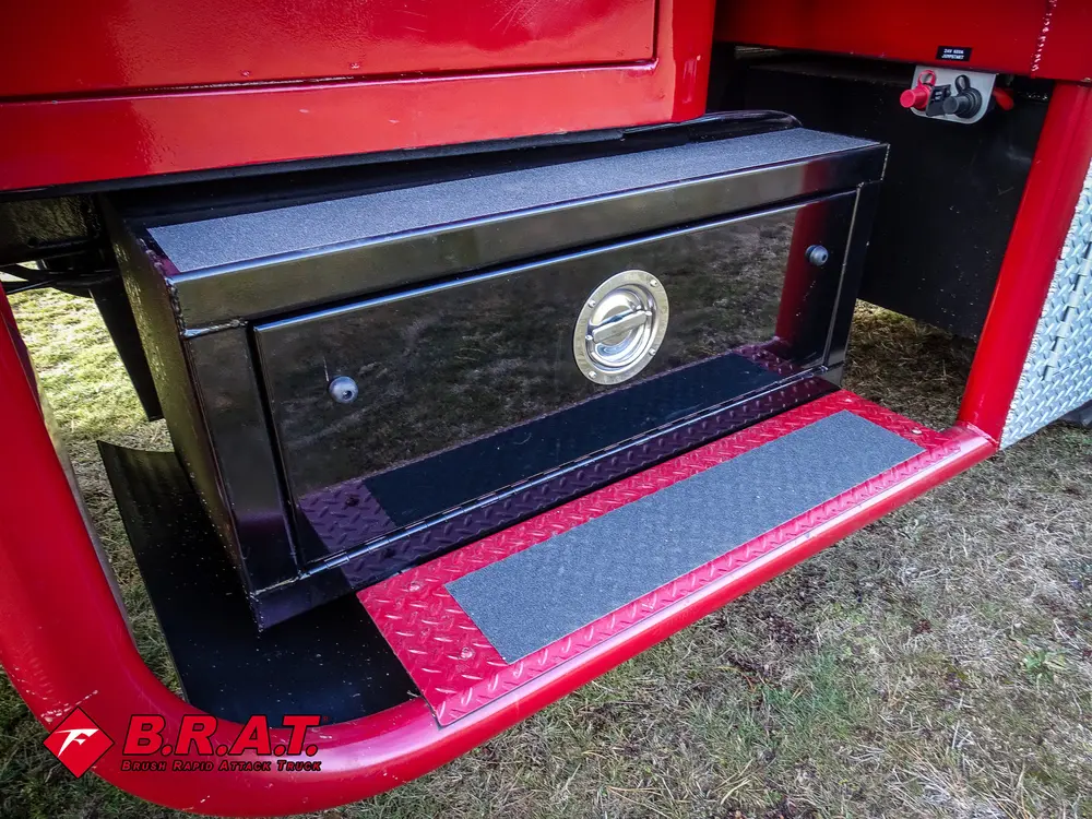 Exterior view of small fire truck showing cab, body compartments, and wheel/tire area.