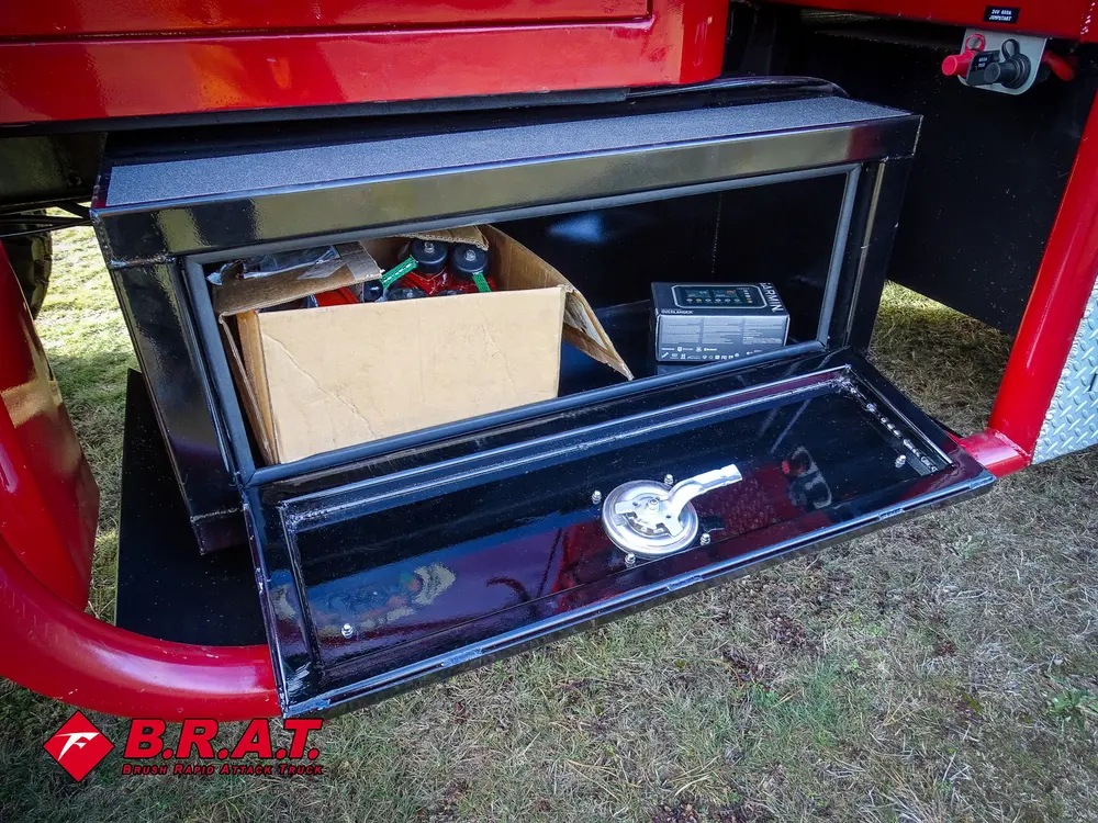 Exterior view of small fire truck showing cab, body compartments, and wheel/tire area.
