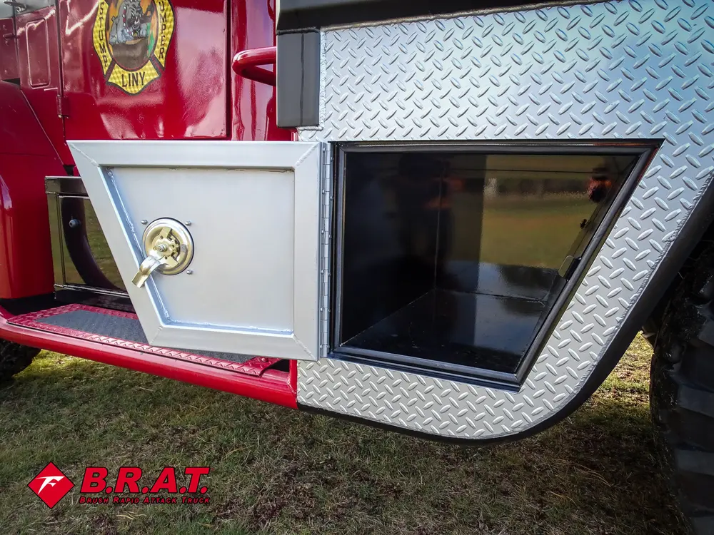 Exterior view of small fire truck showing cab, body compartments, and wheel/tire area.
