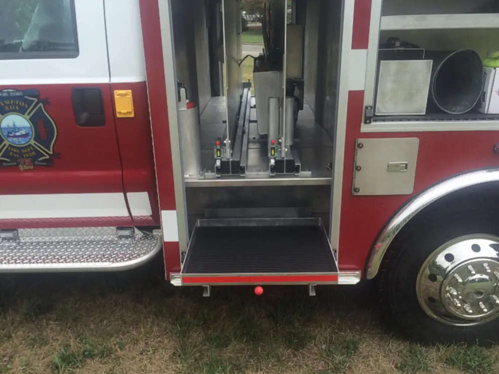 Exterior view of small fire truck showing cab, body compartments, and wheel/tire area.