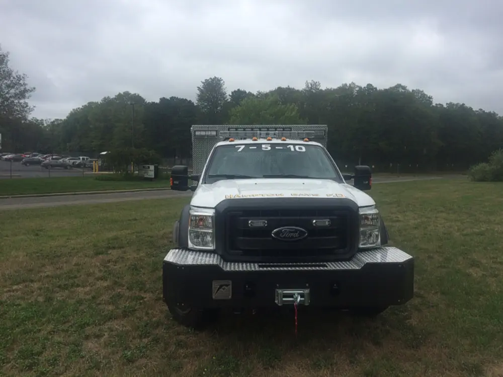 Exterior view of small fire truck showing cab, body compartments, and wheel/tire area.