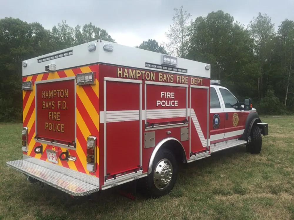 Exterior view of small fire truck showing cab, body compartments, and wheel/tire area.