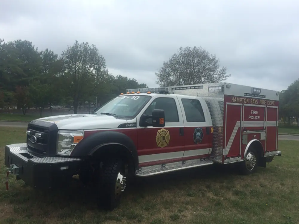 Exterior view of small fire truck showing cab, body compartments, and wheel/tire area.