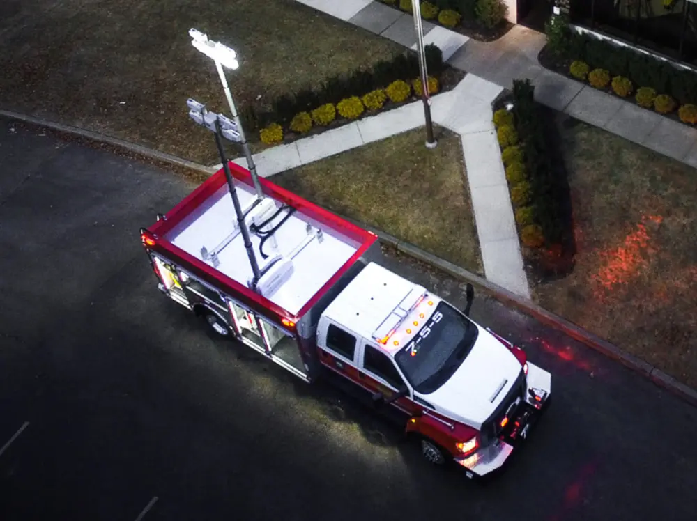 Exterior view of small fire truck showing cab, body compartments, and wheel/tire area.