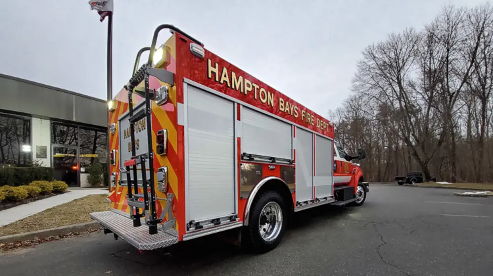 Exterior view of small fire truck showing cab, body compartments, and wheel/tire area.