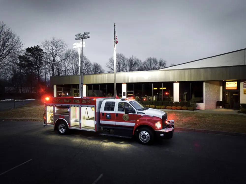 Exterior view of small fire truck showing cab, body compartments, and wheel/tire area.