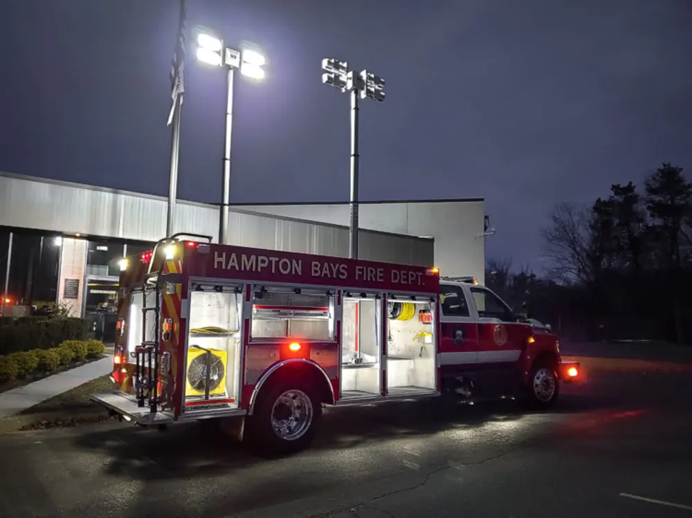 Exterior view of small fire truck showing cab, body compartments, and wheel/tire area.