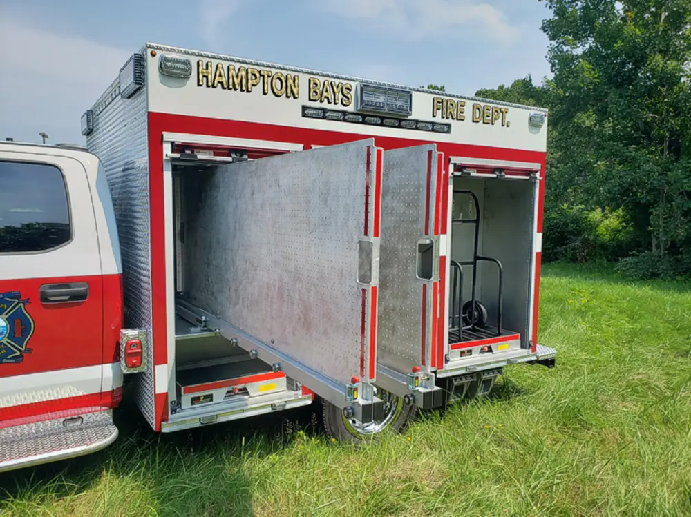 Exterior view of small fire truck showing cab, body compartments, and wheel/tire area.