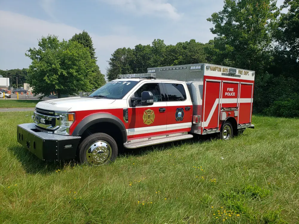 Exterior view of small fire truck showing cab, body compartments, and wheel/tire area.