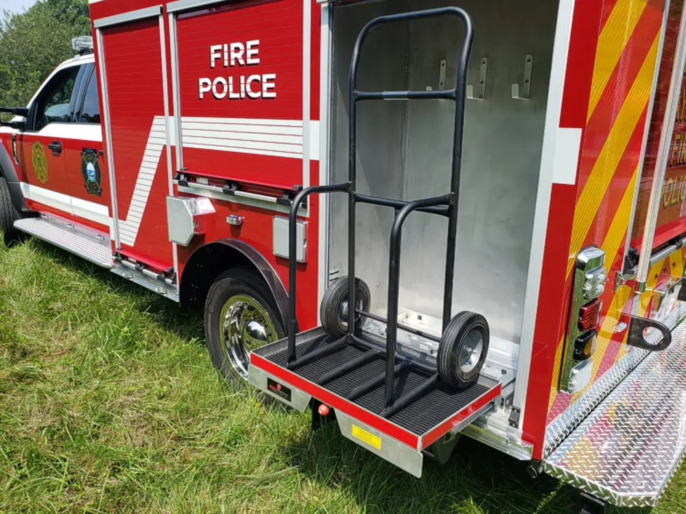 Exterior view of small fire truck showing cab, body compartments, and wheel/tire area.