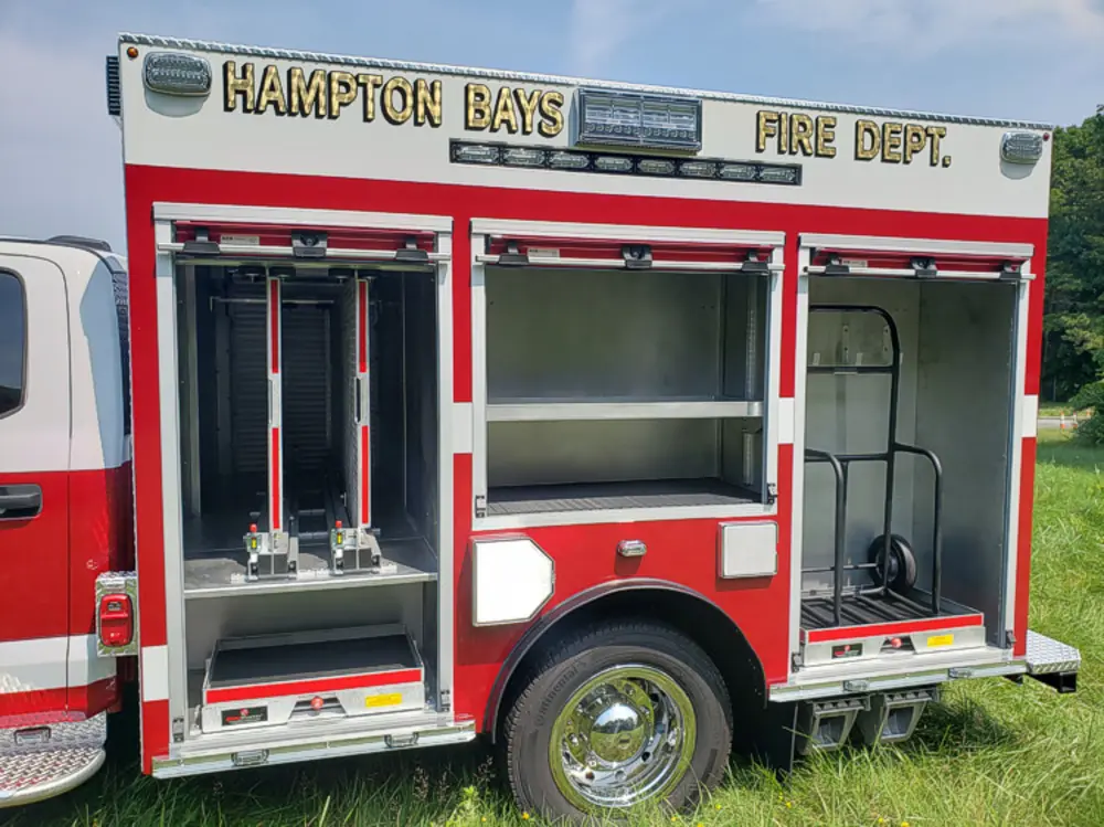 Exterior view of small fire truck showing cab, body compartments, and wheel/tire area.