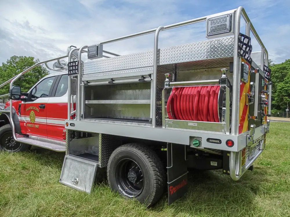 Exterior view of small fire truck showing cab, body compartments, and wheel/tire area.