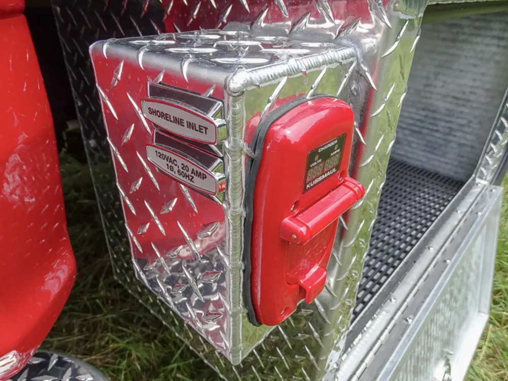 Exterior view of small fire truck showing cab, body compartments, and wheel/tire area.