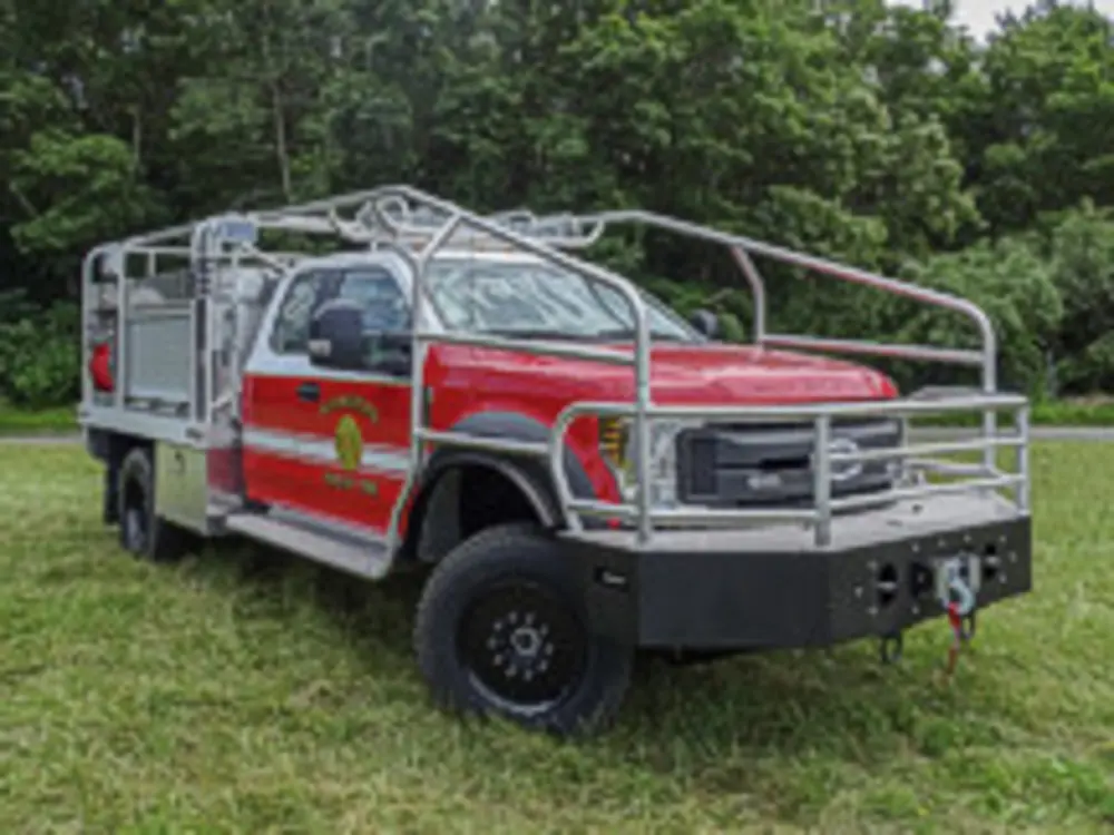 Exterior view of small fire truck showing cab, body compartments, and wheel/tire area.