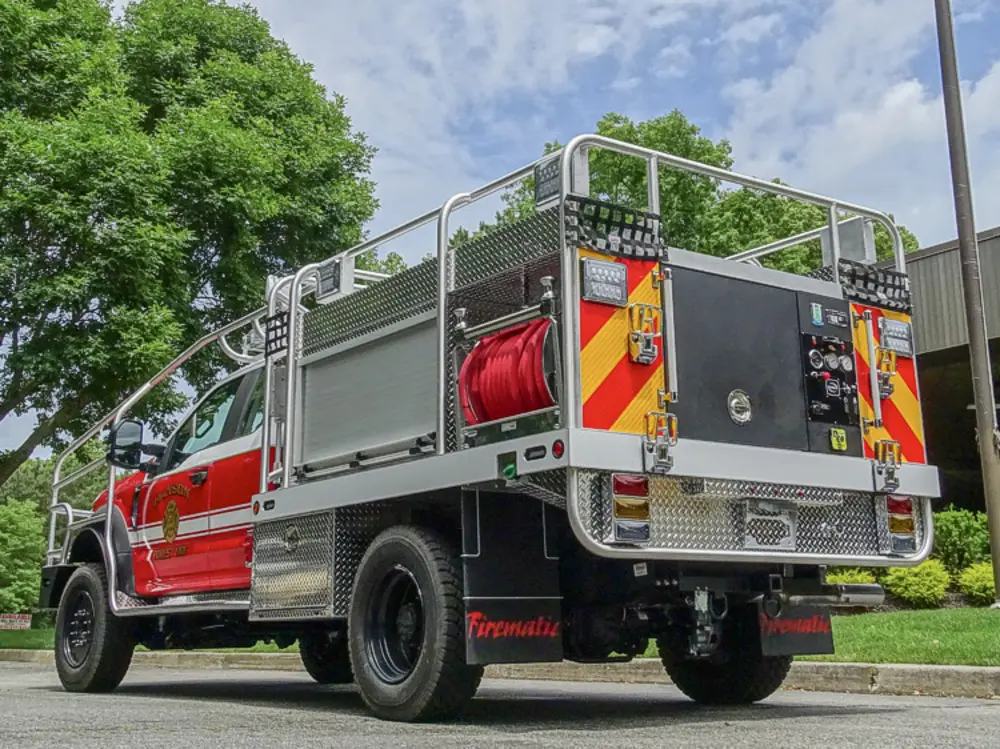 Exterior view of small fire truck showing cab, body compartments, and wheel/tire area.