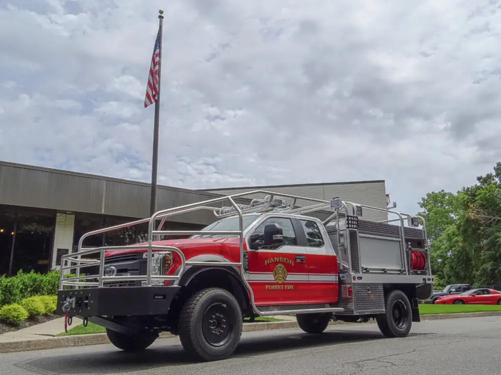 Exterior view of small fire truck showing cab, body compartments, and wheel/tire area.