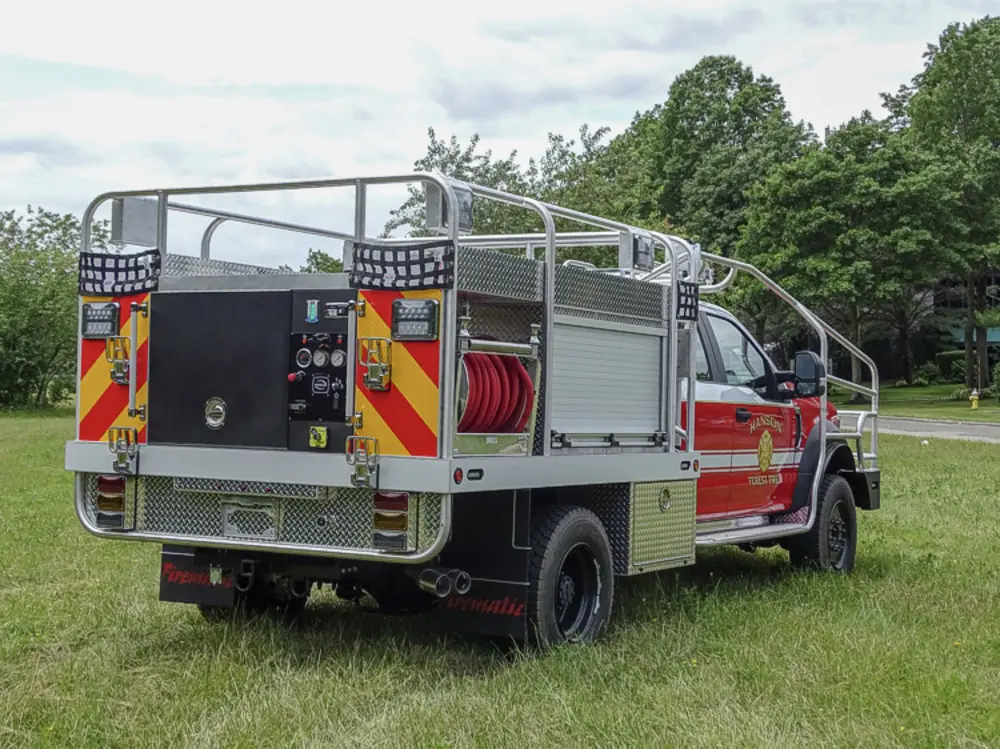 Exterior view of small fire truck showing cab, body compartments, and wheel/tire area.