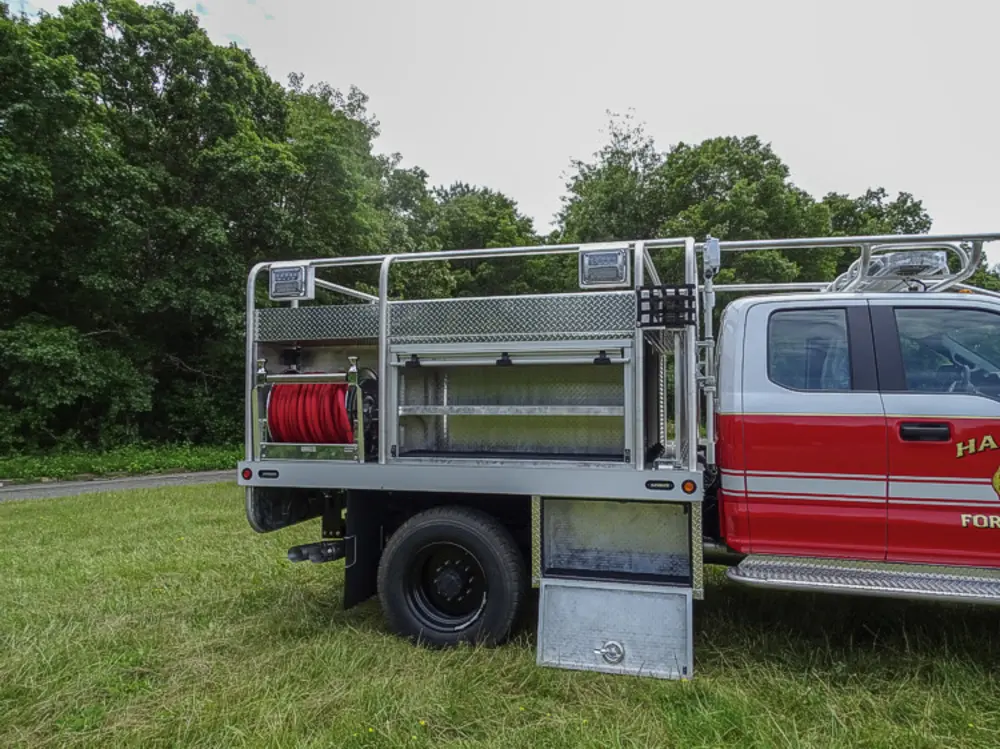 Exterior view of small fire truck showing cab, body compartments, and wheel/tire area.