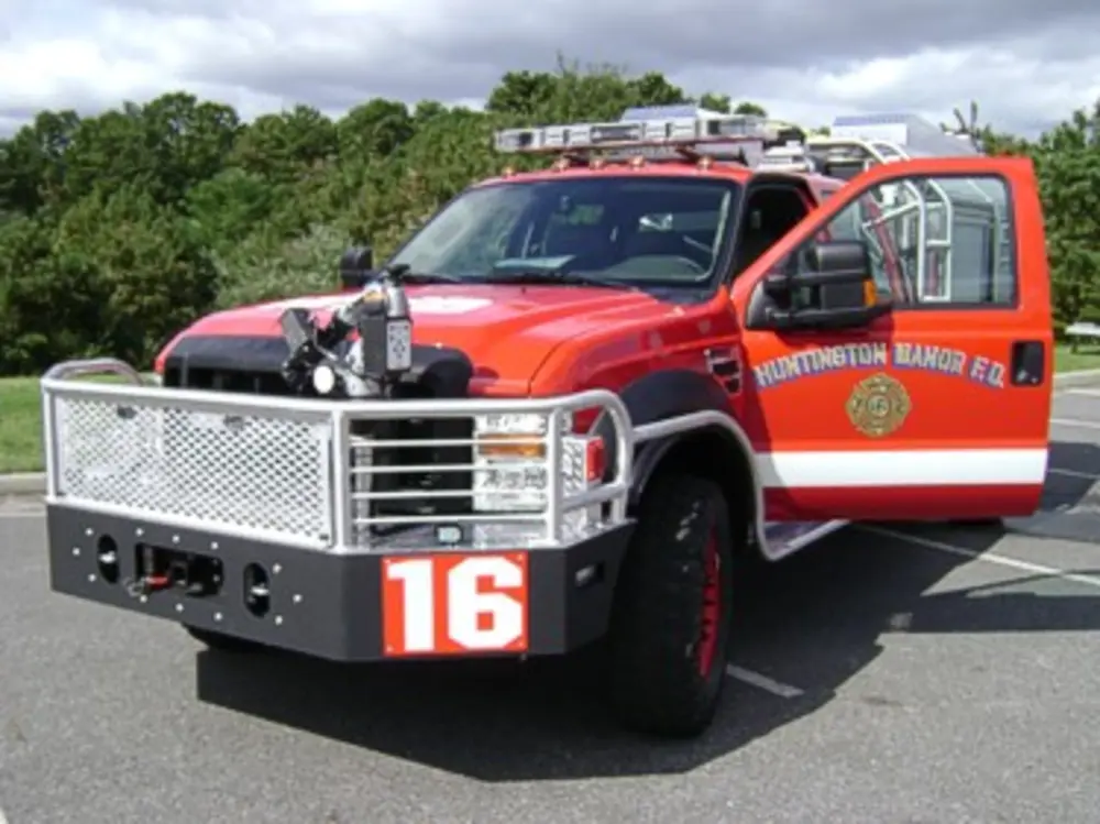 Exterior view of small fire truck showing cab, body compartments, and wheel/tire area.