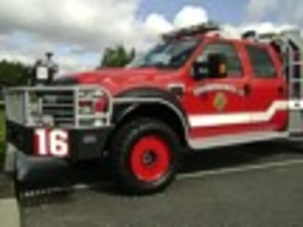 Exterior view of small fire truck showing cab, body compartments, and wheel/tire area.