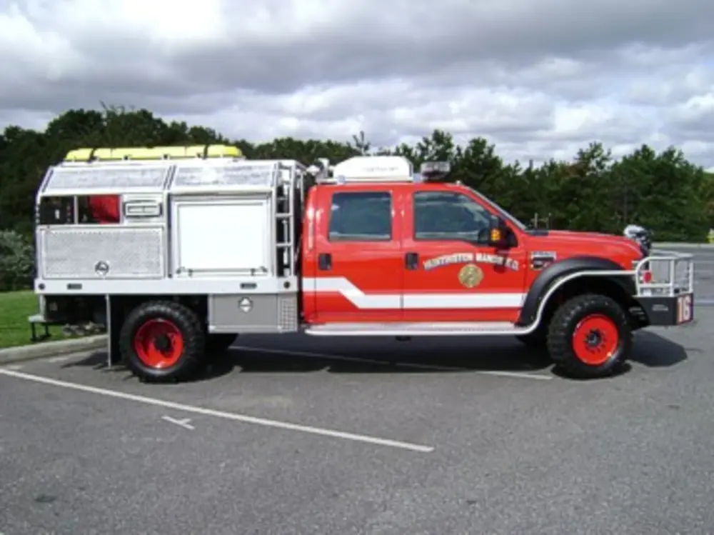 Exterior view of small fire truck showing cab, body compartments, and wheel/tire area.