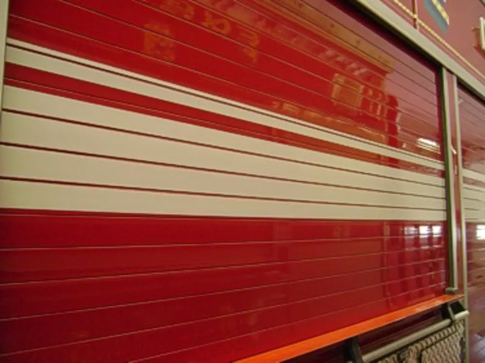 Exterior view of small fire truck showing cab, body compartments, and wheel/tire area.