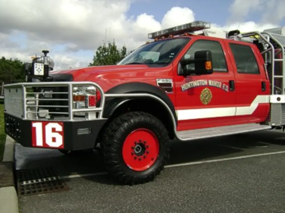 Exterior view of small fire truck showing cab, body compartments, and wheel/tire area.