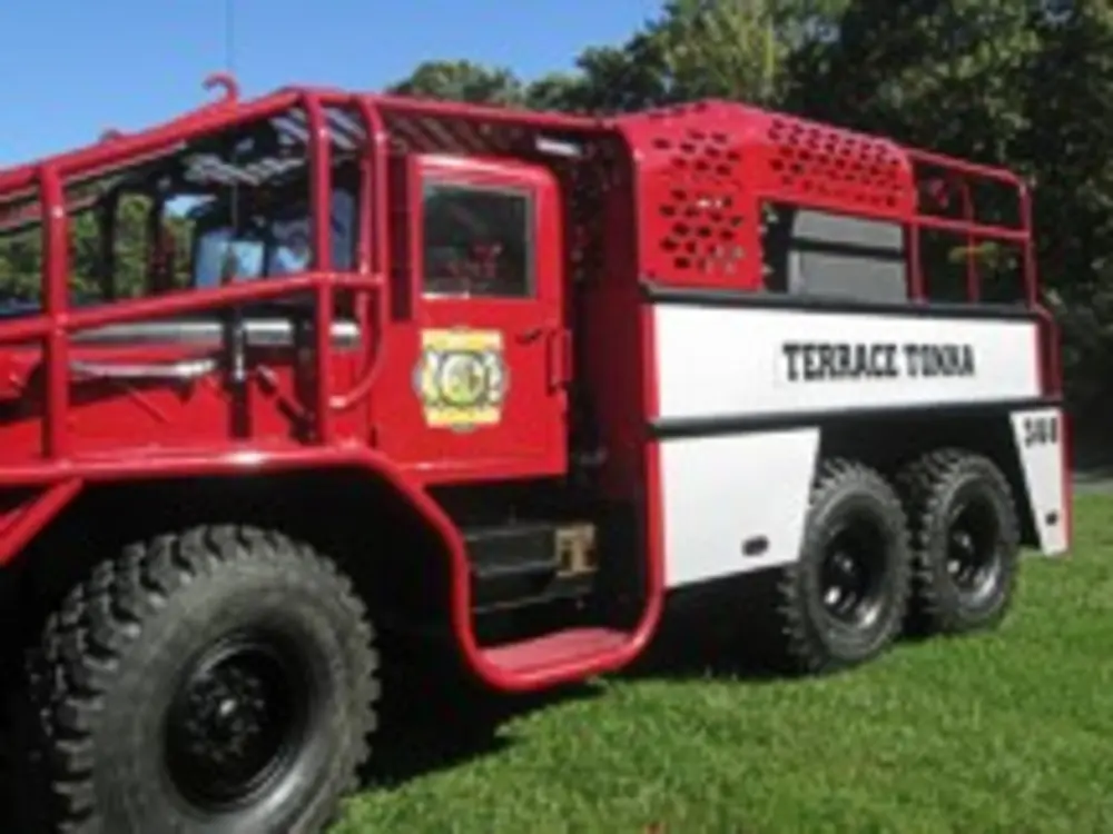 Exterior view of small fire truck showing cab, body compartments, and wheel/tire area.