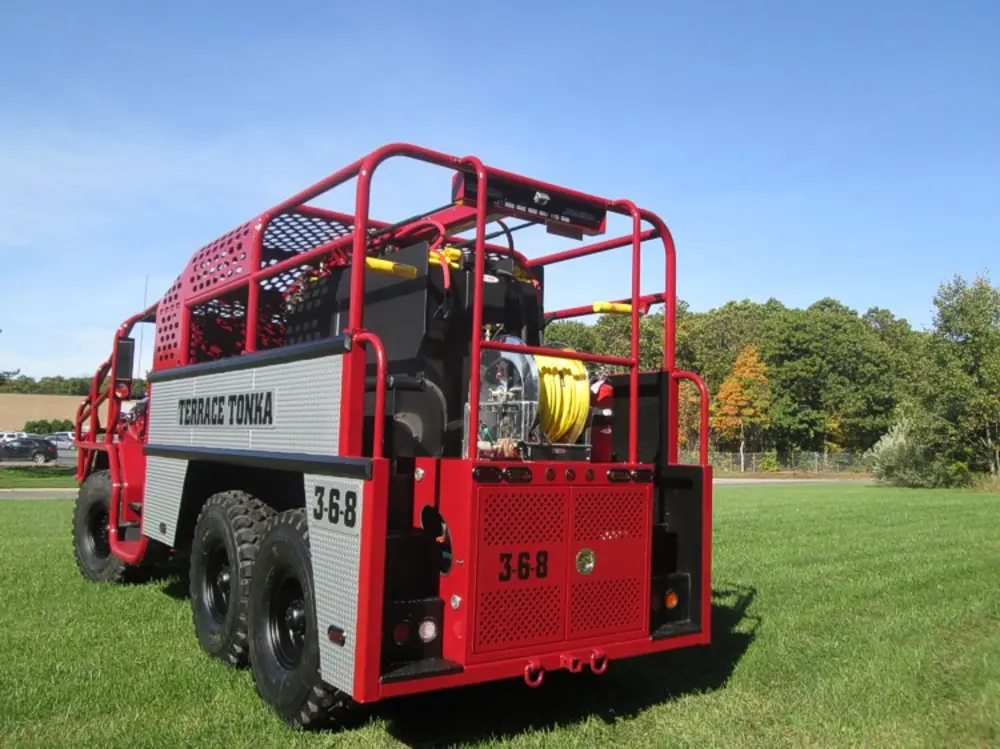 Exterior view of small fire truck showing cab, body compartments, and wheel/tire area.