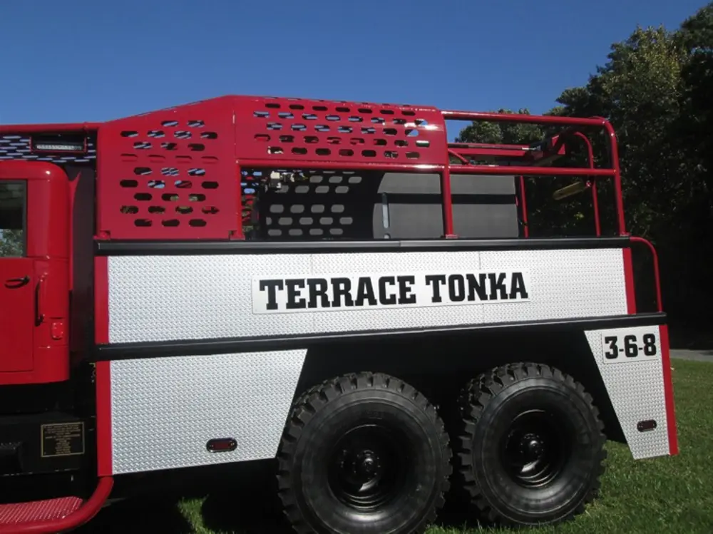Exterior view of small fire truck showing cab, body compartments, and wheel/tire area.
