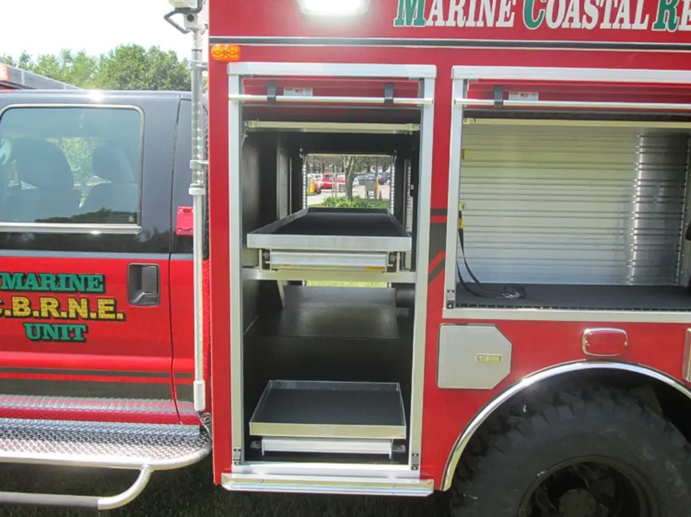 Exterior view of small fire truck showing cab, body compartments, and wheel/tire area.