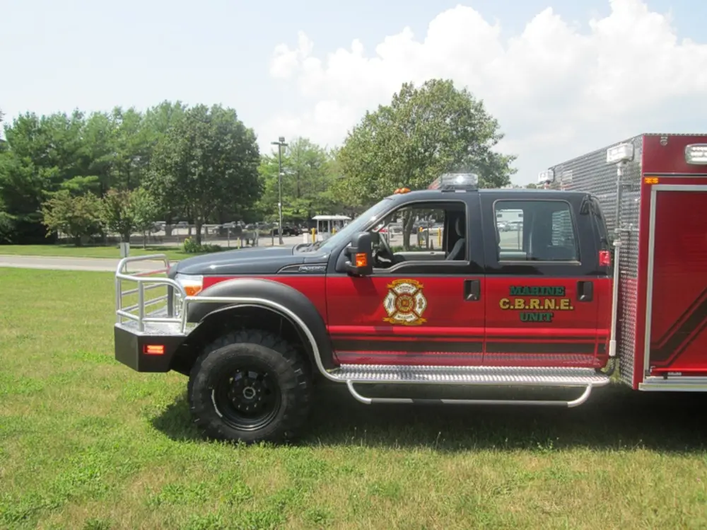Exterior view of small fire truck showing cab, body compartments, and wheel/tire area.