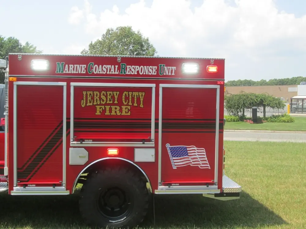 Exterior view of small fire truck showing cab, body compartments, and wheel/tire area.